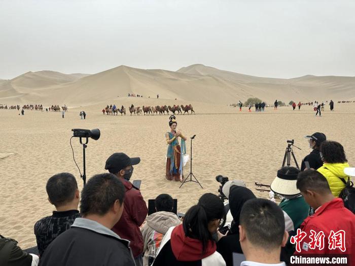 圖為2023年4月底，敦煌大漠“逐舞者”奧楠在鳴沙山月牙泉景區(qū)視頻直播，吸引游人圍觀?！●T志軍 攝